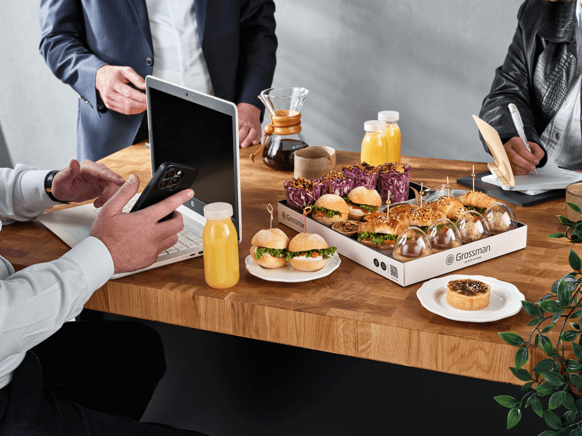 תמונת אווירה של משרד שלושה אנשים סביב שולחן עם מארז מיקס פינגר פוד